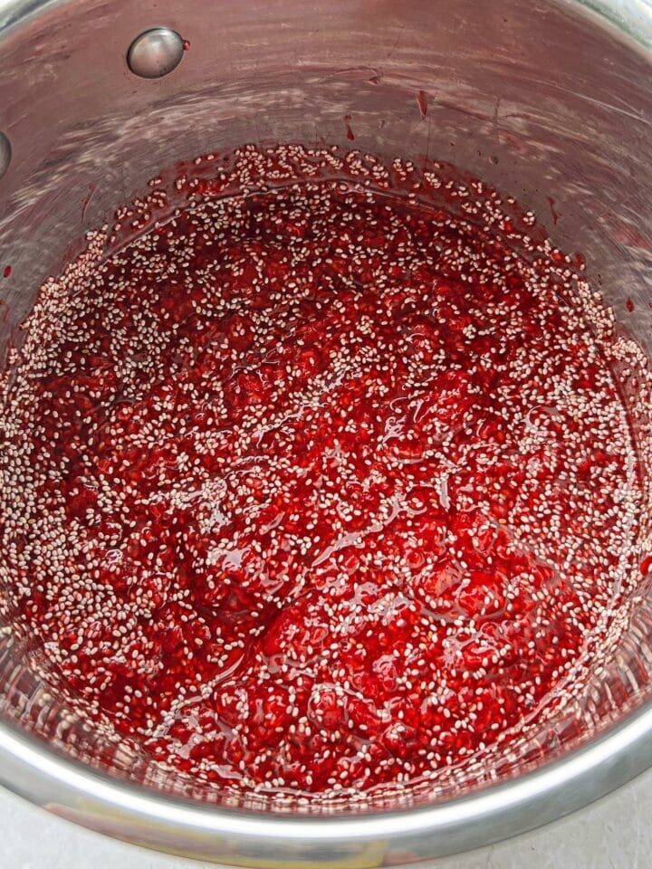 Chia seeds added to a saucepan with mashed cooked raspberries.