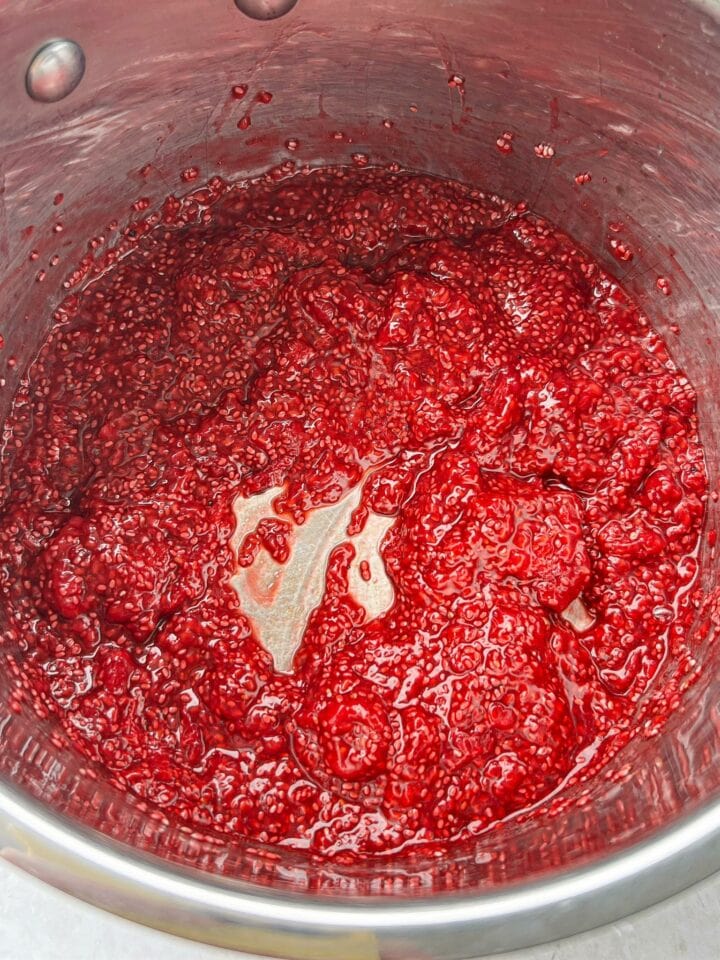 Plump chia seeds mixed into cooked raspberries. The mixture is thick, like jam. 