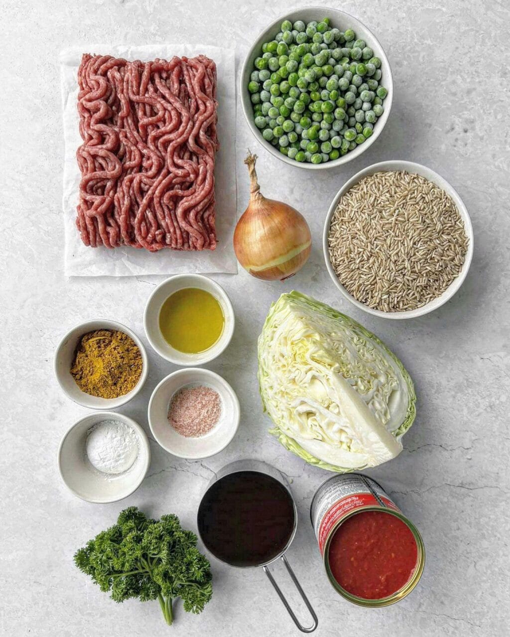 A birdseye photo of ingredients to make curried rice, including mince, peas, onion, spices, salt, oil, cornflour, rice, cabbage, canned tomatoes, beef stock and parsley.