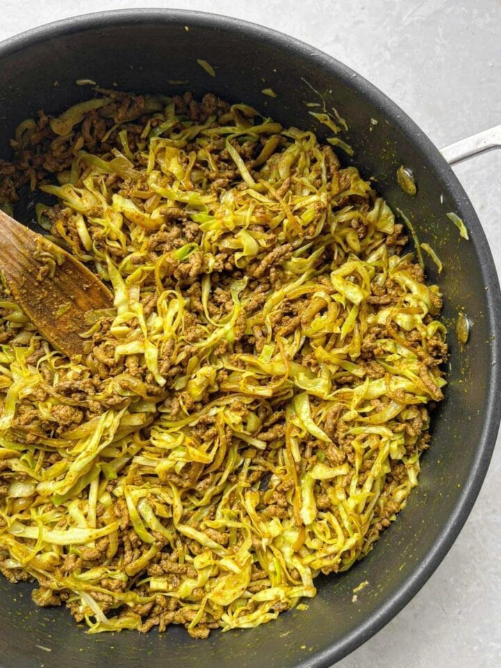 Sautéd beef mince with shredded slightly wilted cabbage and curry powder in a large deep fry pan with a wooden spoon.  