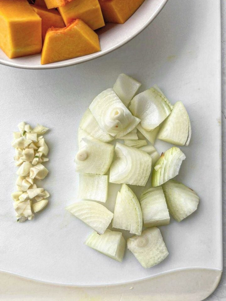 Roughly chopped onion and garlic on a white chopping board.