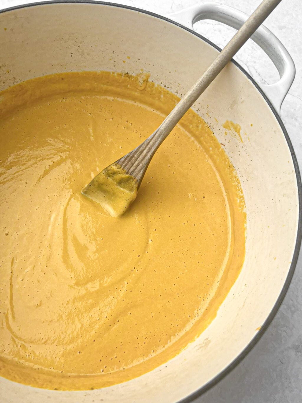 A stove pot with freshly made butternut squash soup, with a wooden spoon inserted for mixing. 
