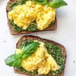 A picture of two slices of toast topped with scrambled eggs and pesto.