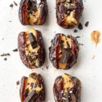 Medjool dates sliced and filled with peanut butter and dark chocolate on a white plate.