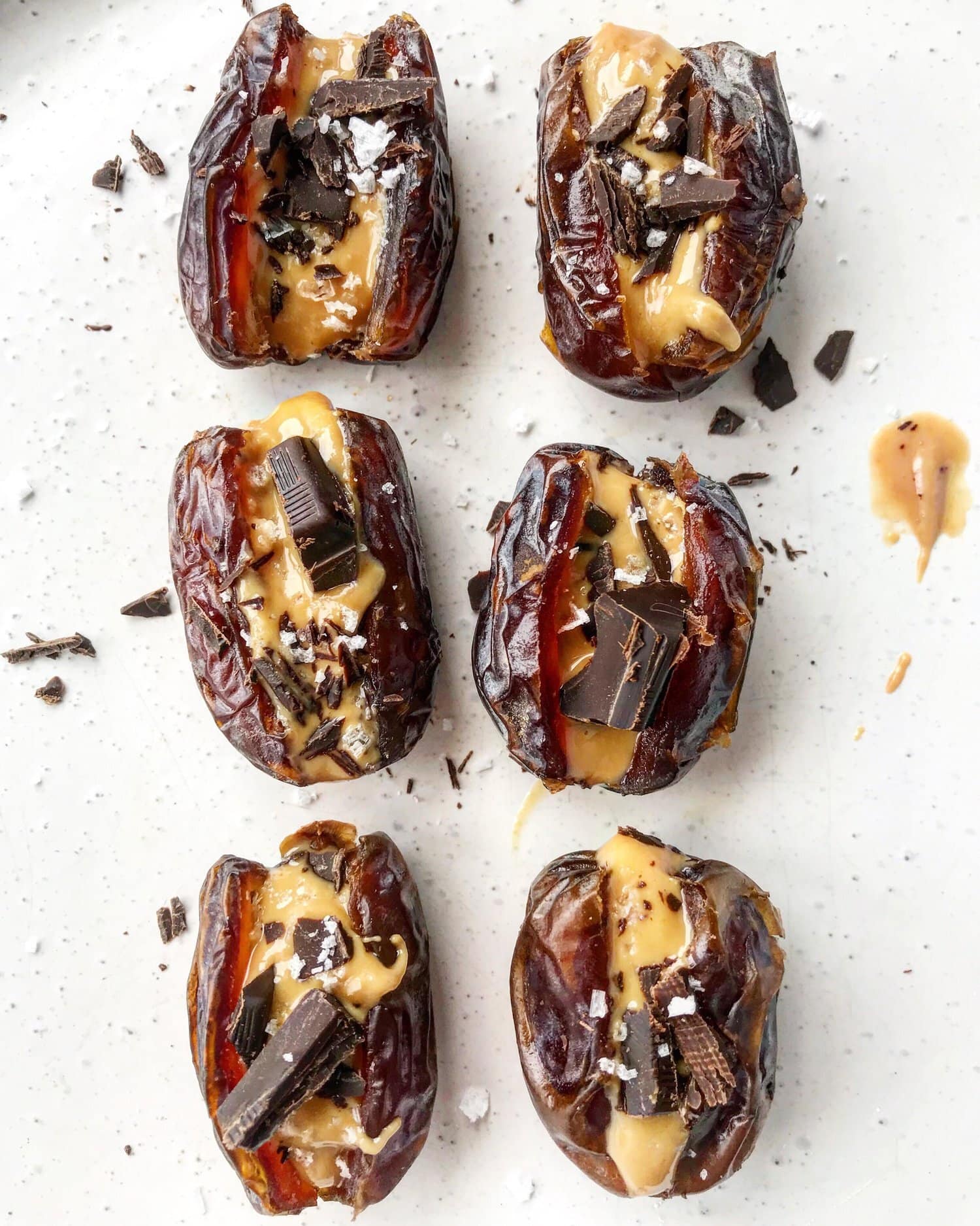 Medjool dates sliced and filled with peanut butter and dark chocolate on a white plate.