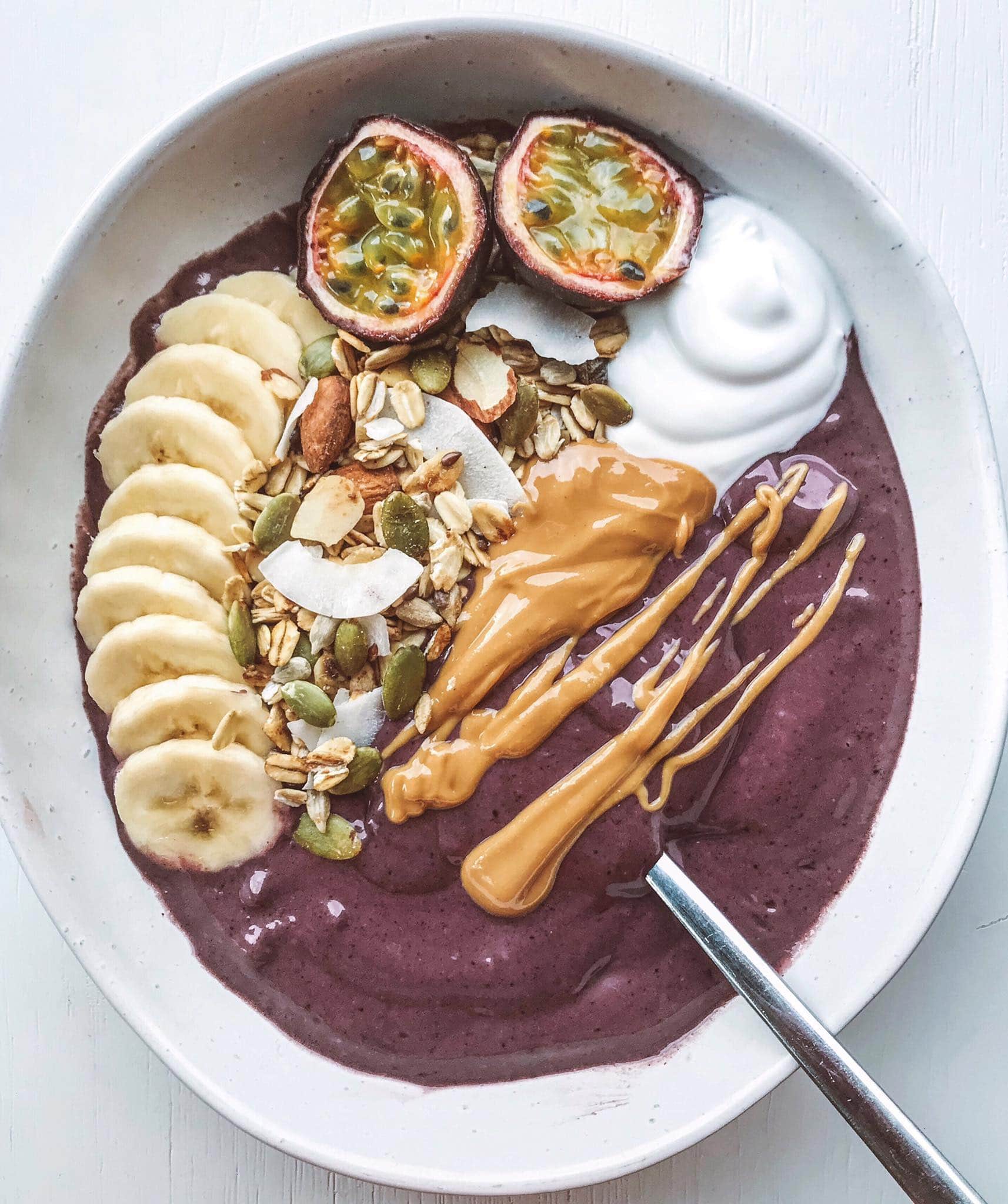 Berry acai bowl served topped wth peanut butter, yoghurt, muesli and fruit.