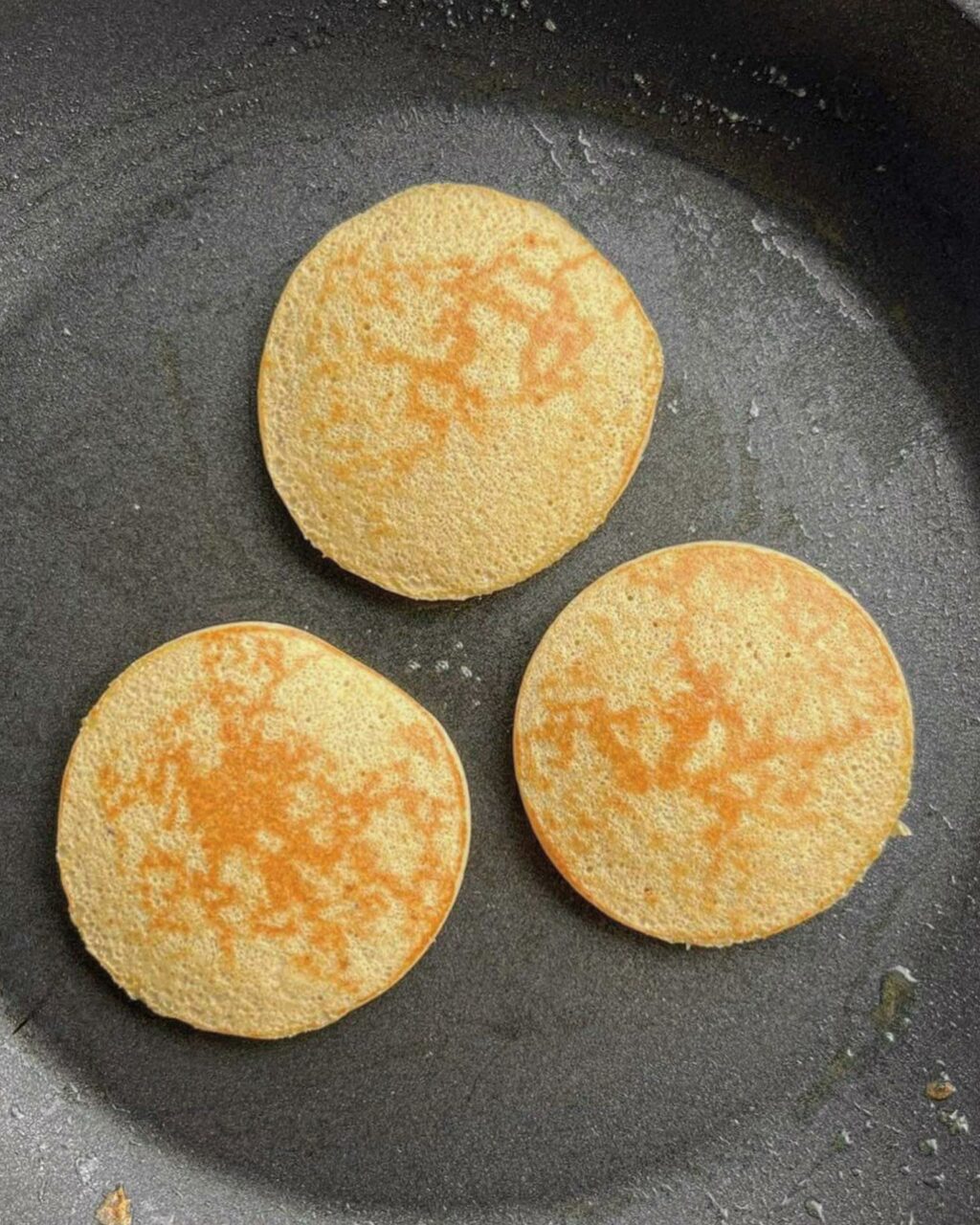 A photo of three cooked protein pancakes in a black pan.