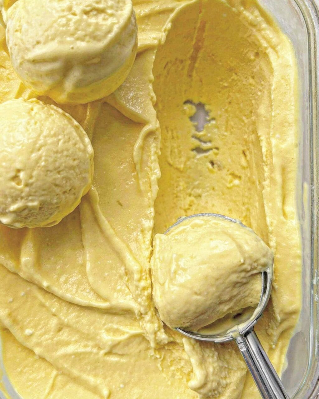 A close up of mango coconut milk ice cream showing 3 ice cream balls and a ice cream scoop. 