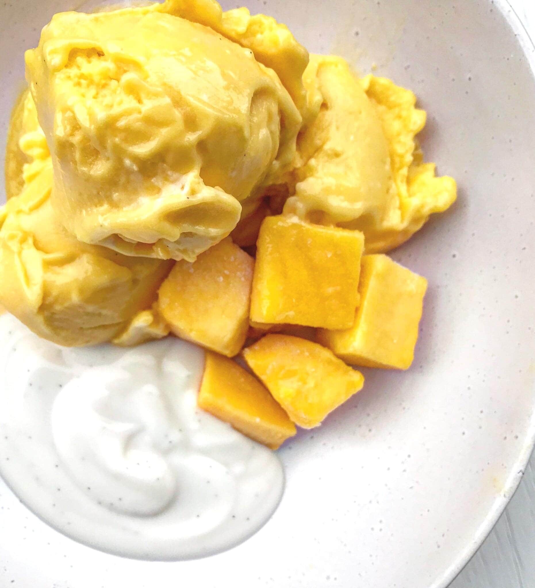 A bowl of mango coconut vegan ice cream served with coconut yoghurt and cubed mango.