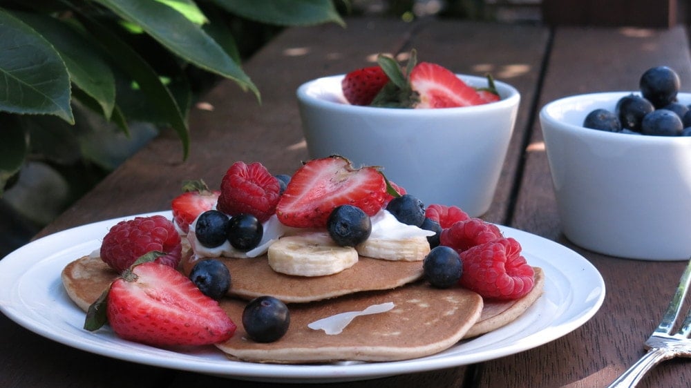 Stack of banana oat pancakes topped with fruit and yoghurt. 