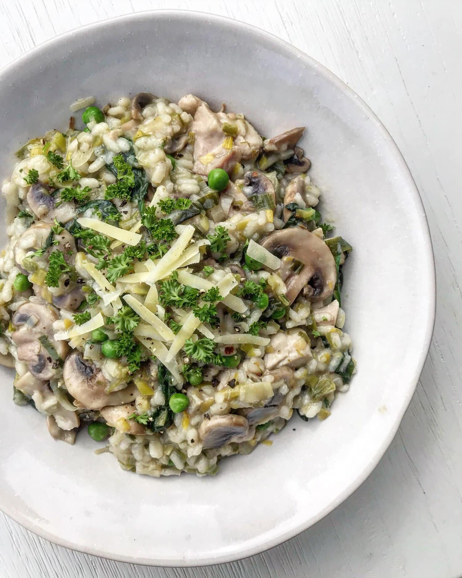 A close up of chicken and leek risotto topped with fresh herbs and grated cheese. 