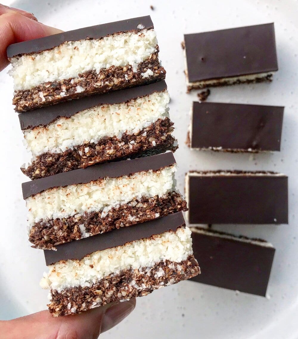 A stack of sliced coconut, chocolate and peppermint slice being held. 