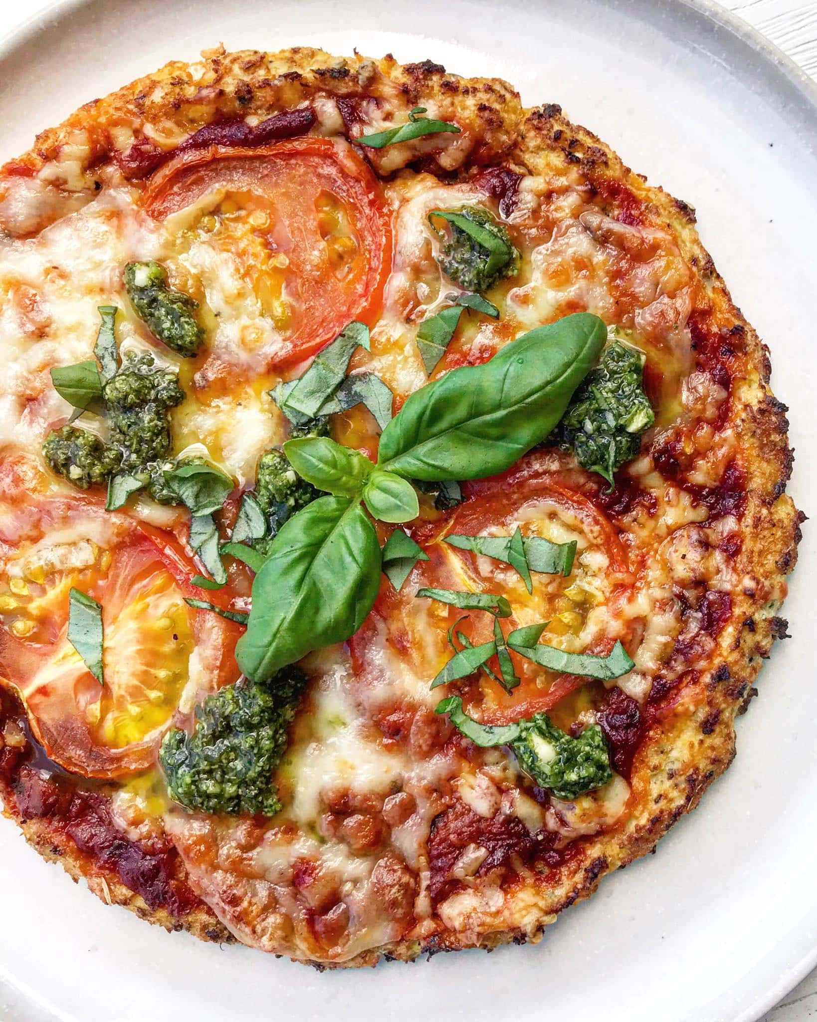 Cauliflower pizza base with tomato, cheese and pesto toppings.