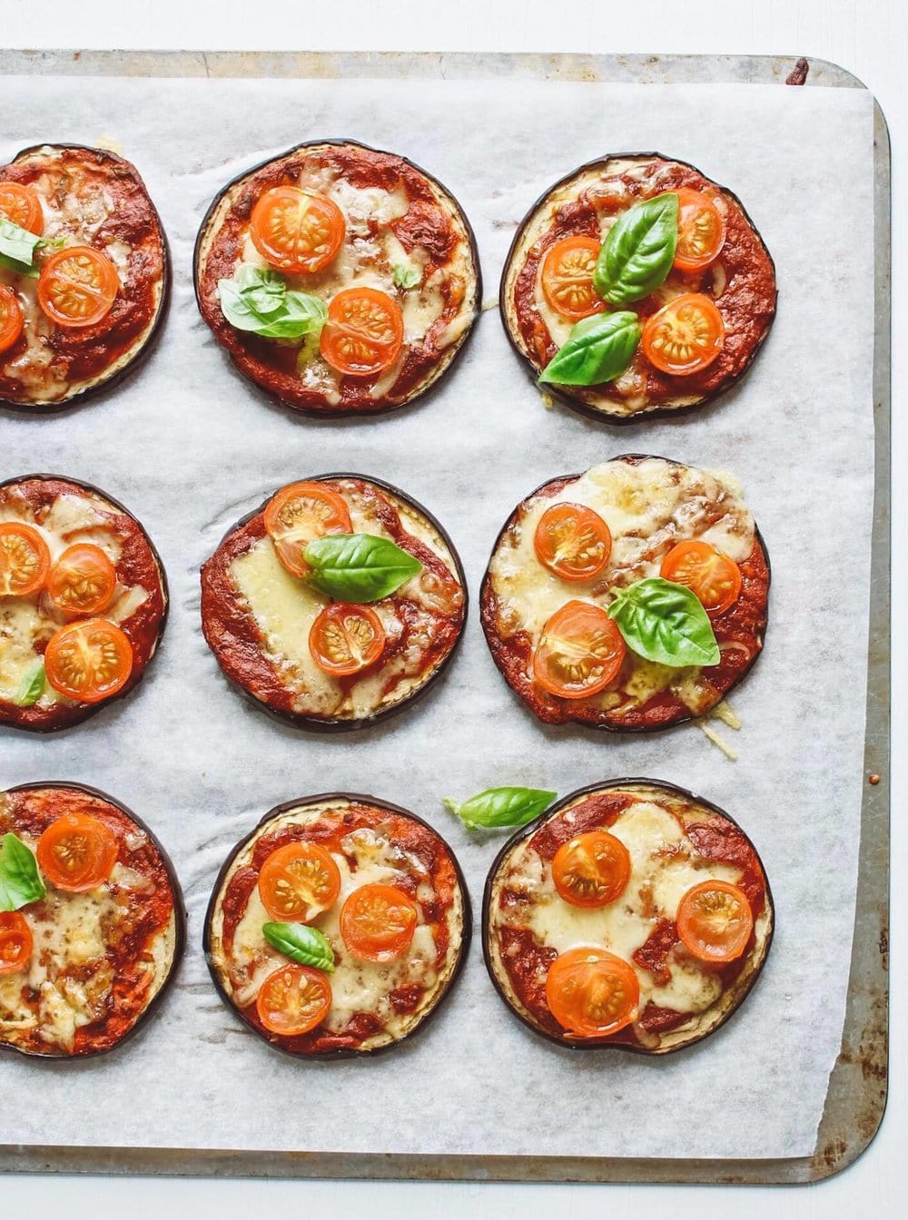 Tray of mini eggplant pizzas garnished with basil. 