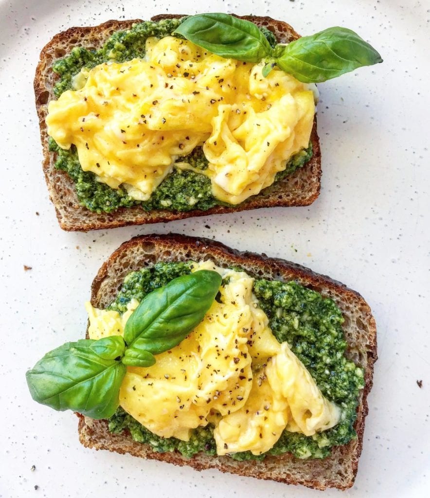 Multigrain toast topped with pesto and scrambled egg, with fresh basil to garnish.