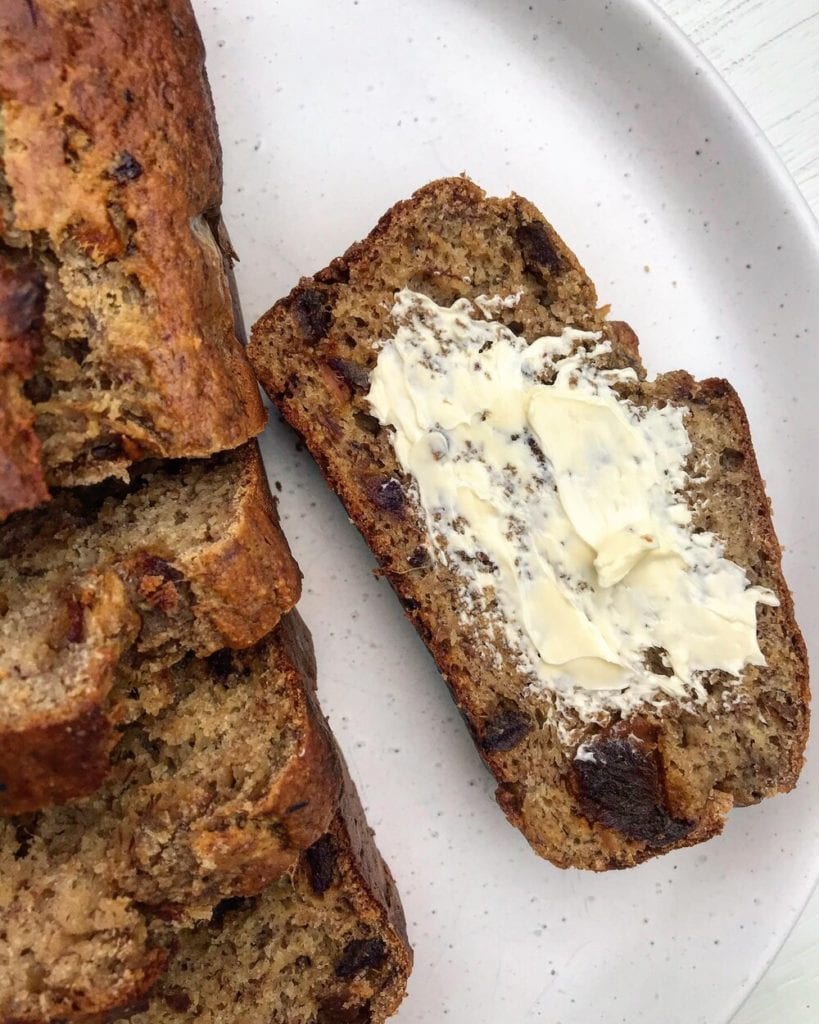 A close up slice of banana date bread spread with butter.