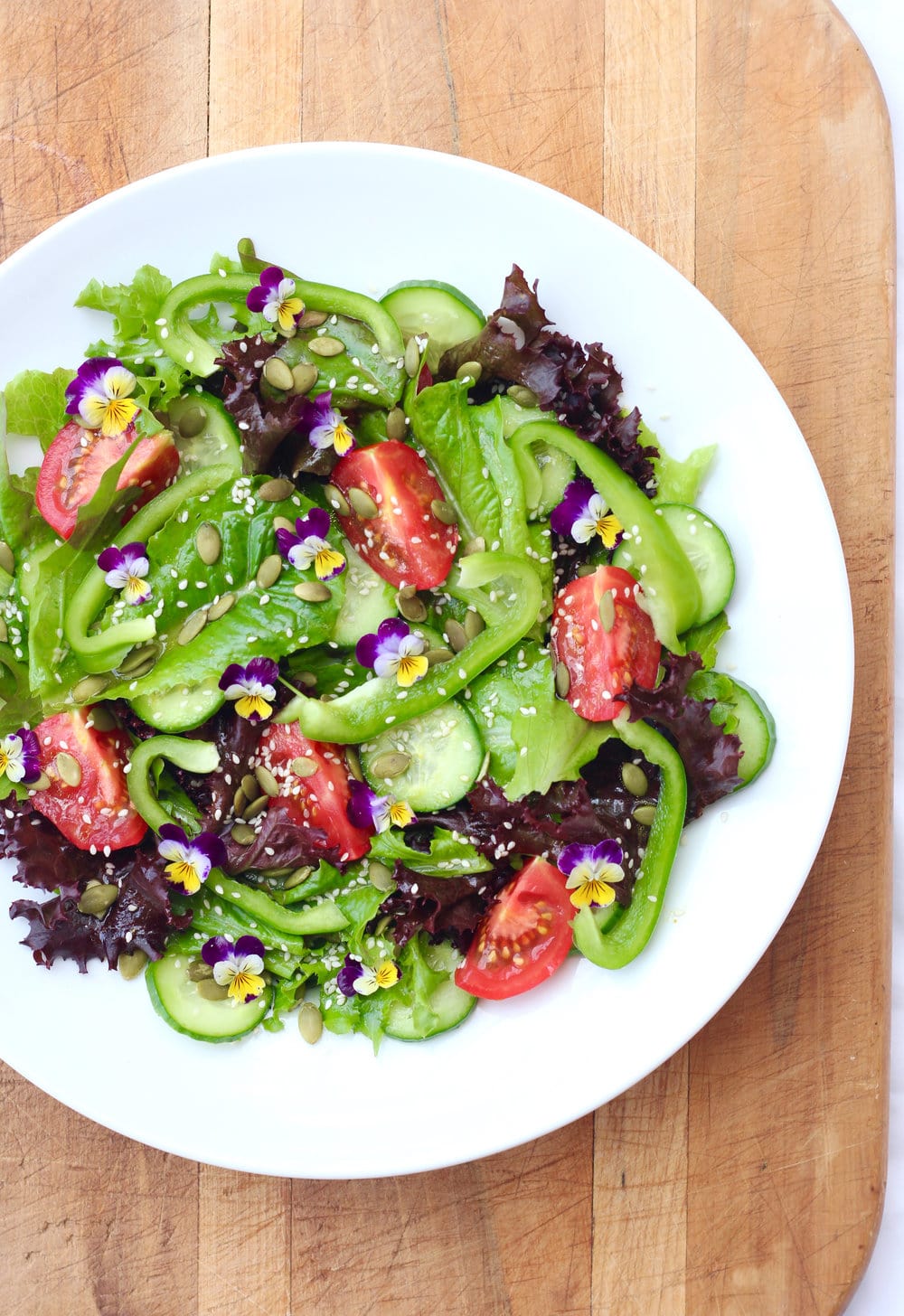 Close up of a garden salad topped with seeds and edible flowers. 