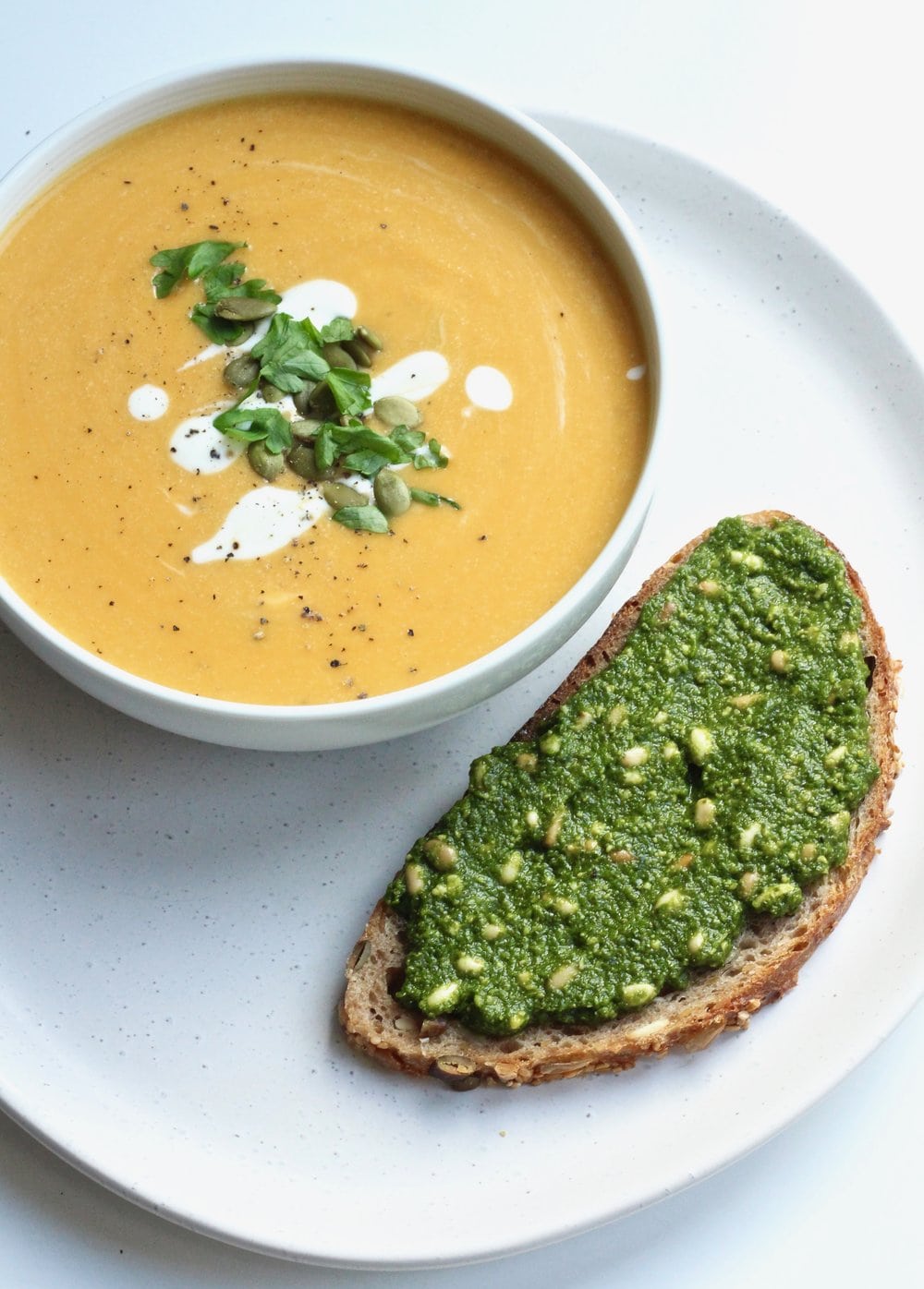 Bowl of vegan cream of pumpkin soup served with pesto covered toast. 