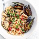 A bowl of mussel tomato pasta topped with fresh herbs.