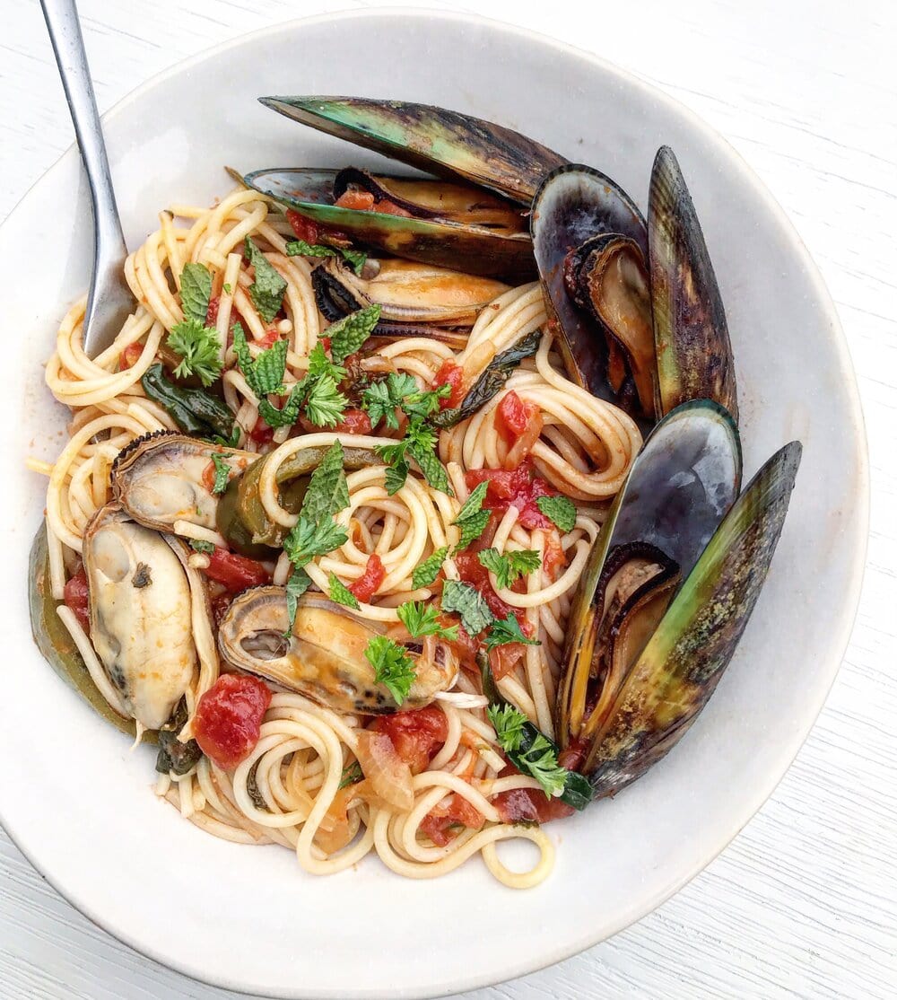 A bowl of mussel tomato pasta topped with fresh herbs.