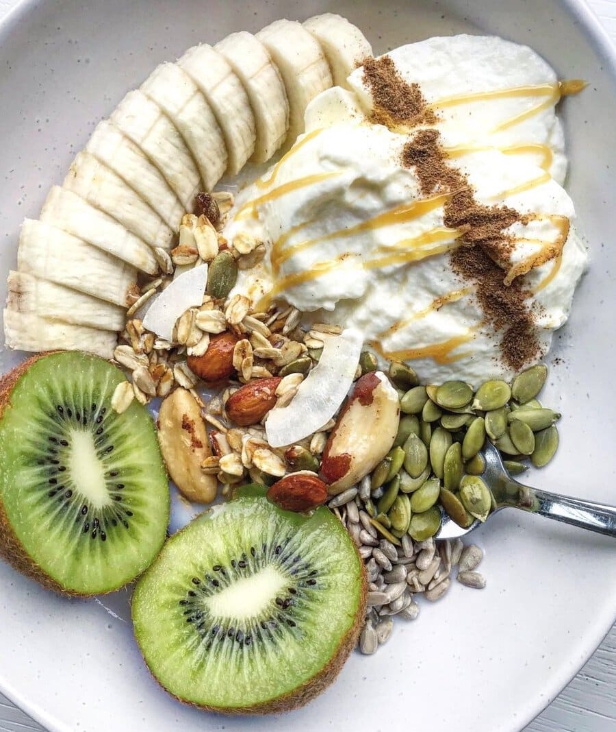 Bowl of fruit, banana, kiwifruit, muesli and seeds.