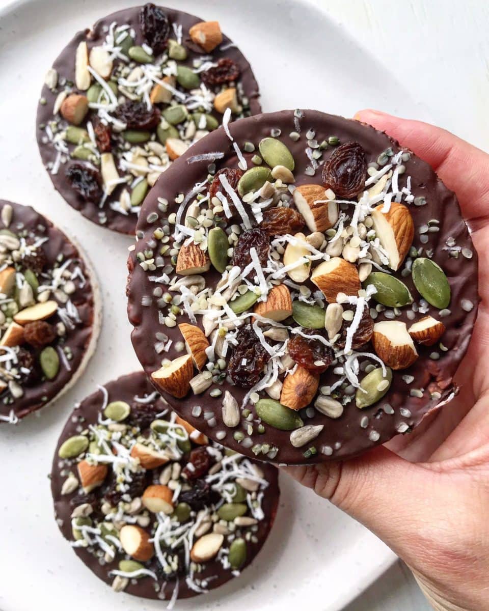 A close up of chocolate-covered rice cakes. The topping includes raisins, seeds, coconut and almonds. 