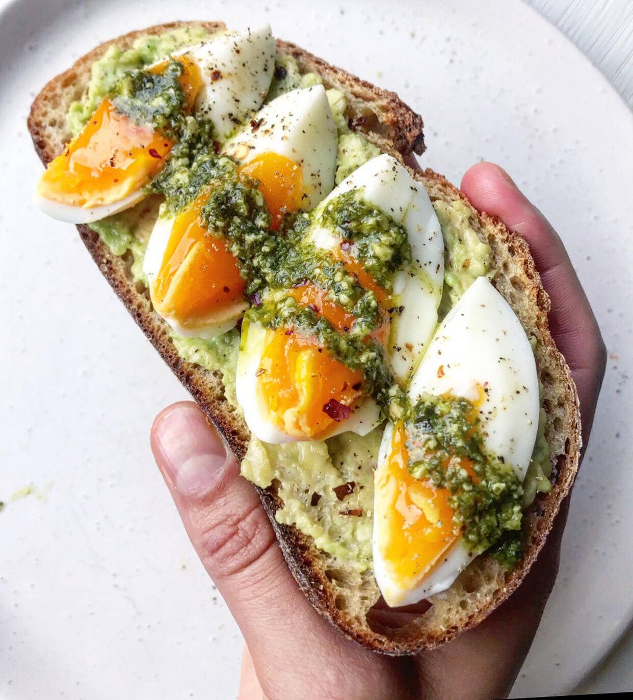 Sourdough bread topped with avocado, boiled egg and pesto.