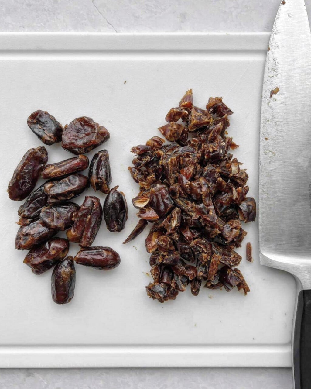 Dates on a chopping board. One pile is whole, the other pile is finely chopped.