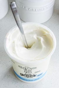 A large tub of yoghurt with a spoon in it.