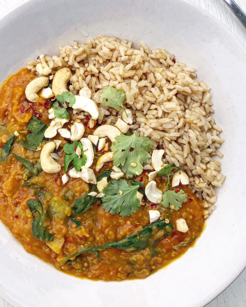 Close up of red lentil dahl topped with cashews, coriander and chili flakes. 