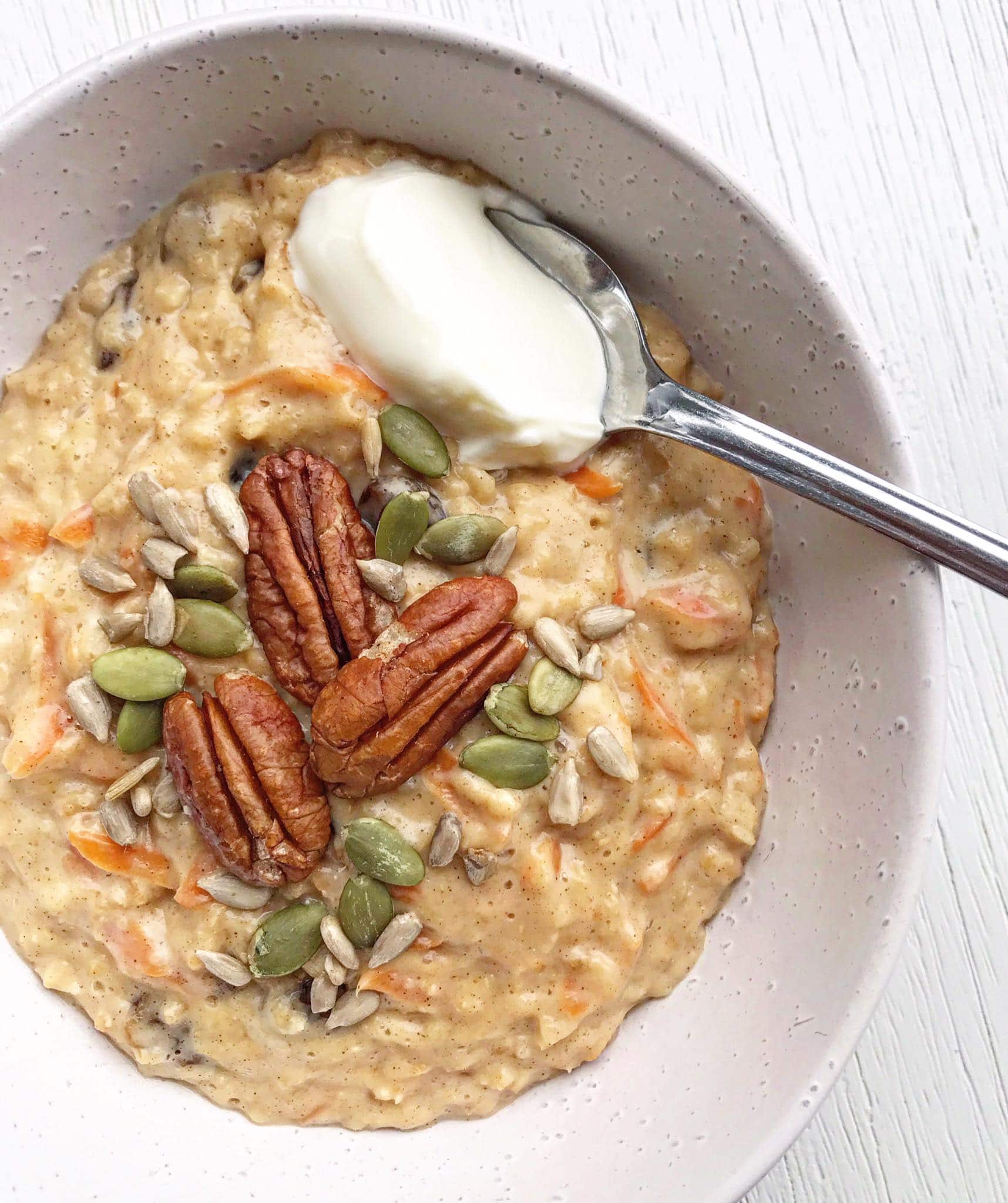 A picture of a bowl of carrot cake porridge topped with pecans, seeds and yoghurt.