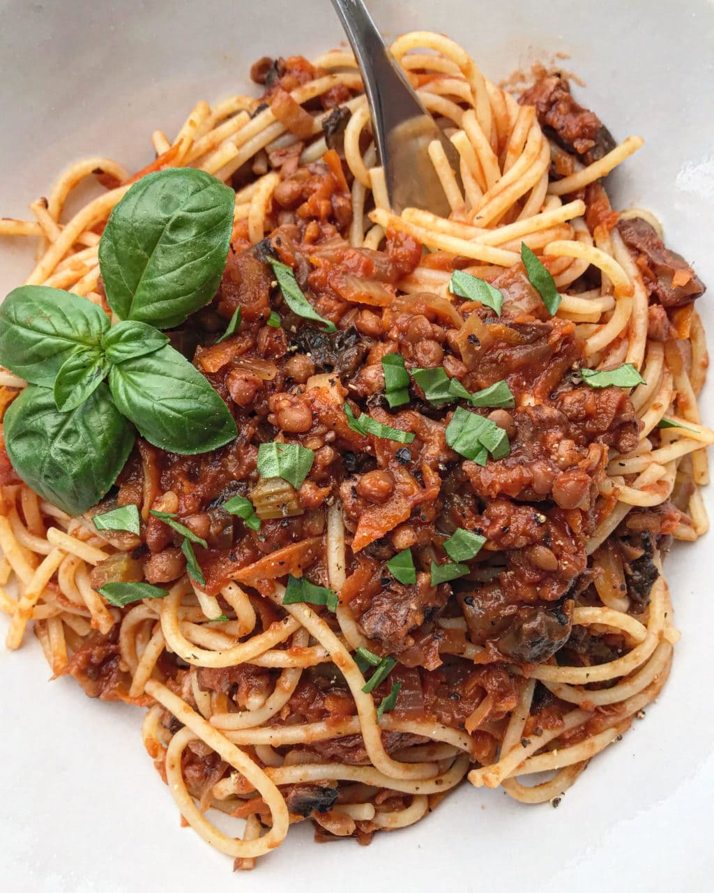 A white bowl with plant-based bolognese sauce overtop of spaghetti pasta. 