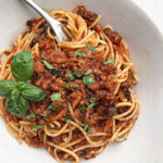 A bowl of vegan bolognese sauce on spaghetti pasta with chopped basil over top