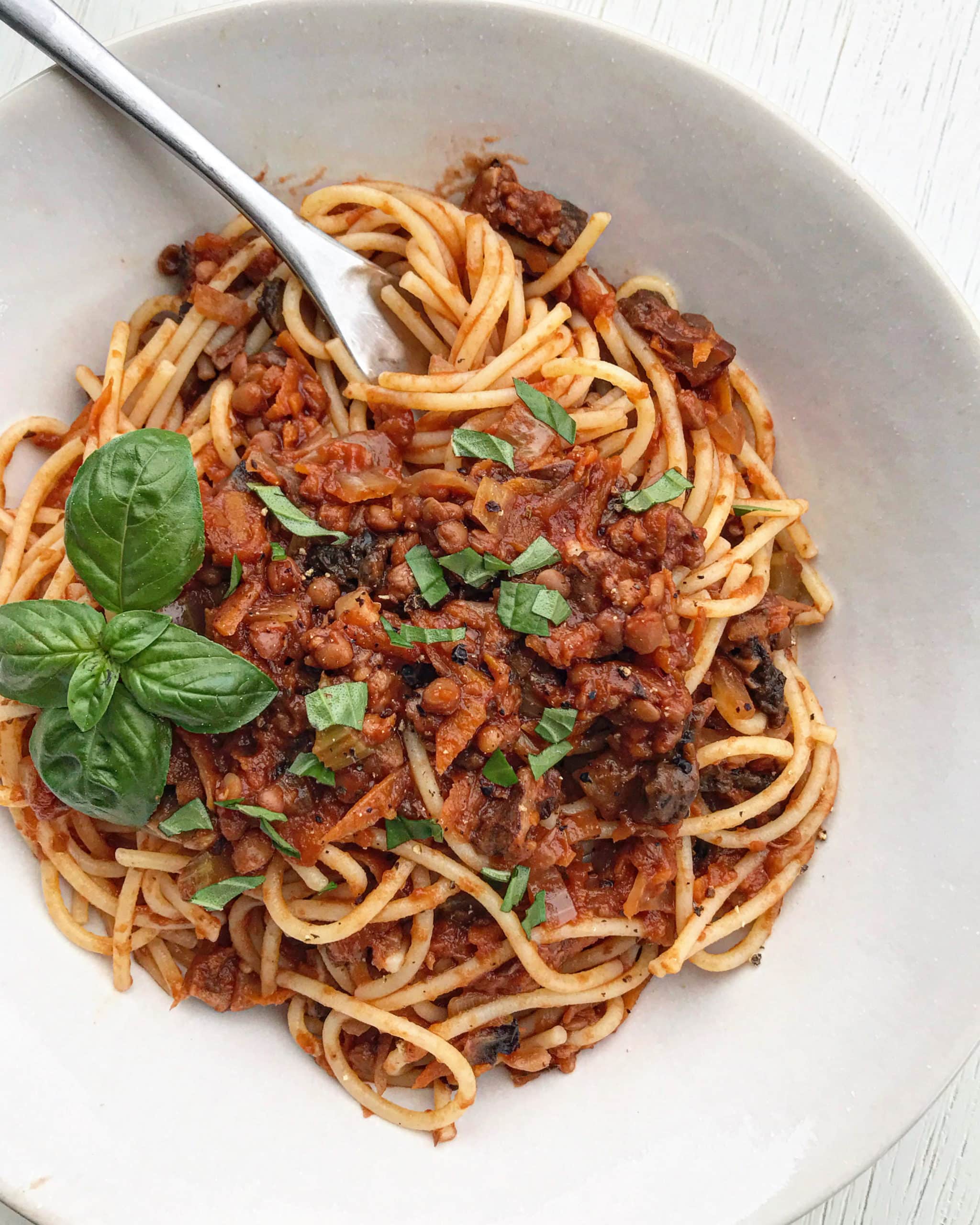 A bowl of vegan bolognese sauce on spaghetti pasta with chopped basil over top