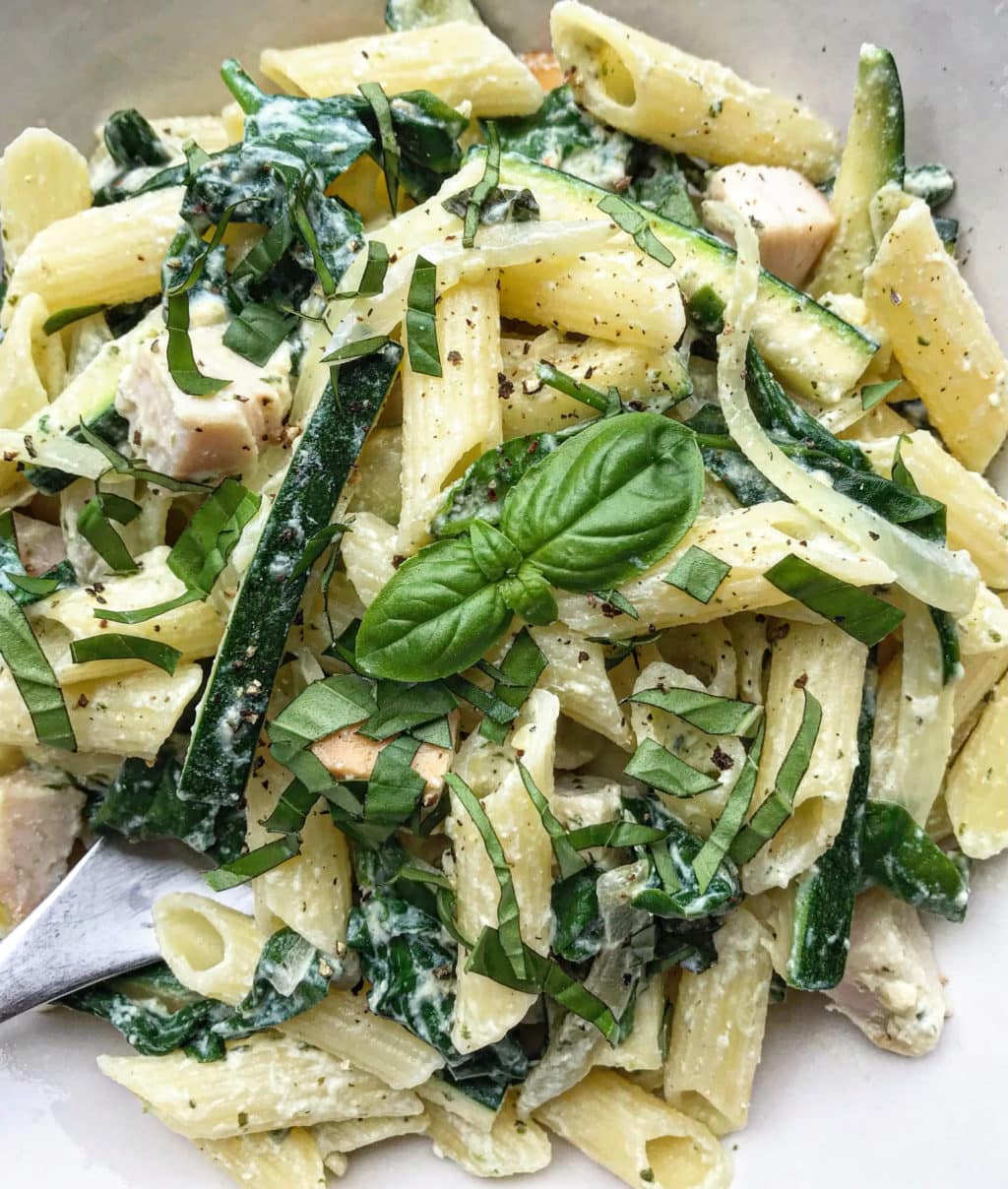 A close up photo of ricotta pesto pasta topped with a fresh basil leaf. 