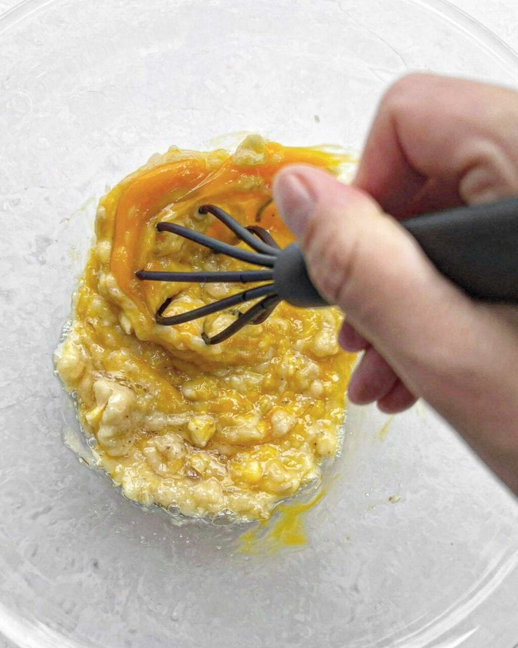 Eggs and vanilla being whisked into mashed banana. 