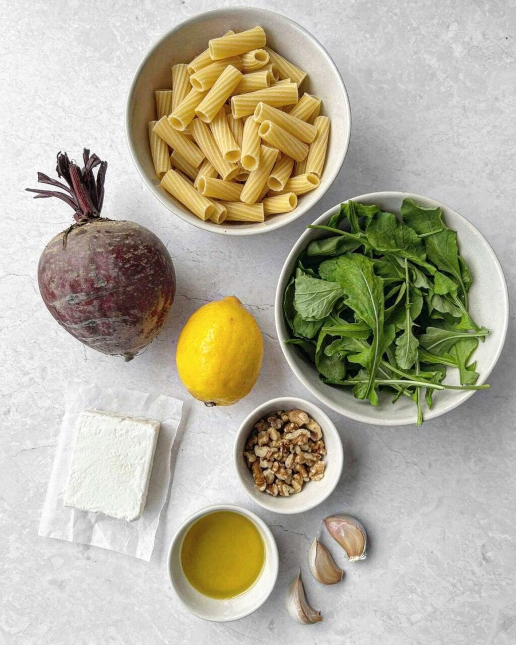 The ingredients needed for beetroot goat cheese pasta, including rigatoni pasta, beetroot, lemon, rocket, goat cheese, walnuts, olive oil and garlic. 