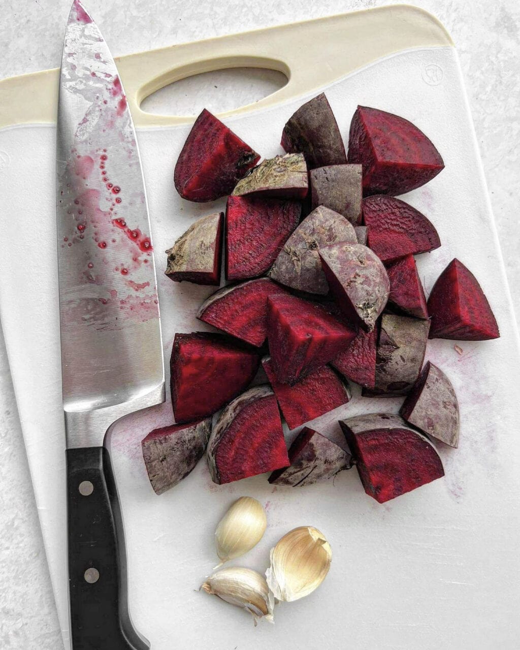 A chopping board with chopped beetroot and garlic cloves. 