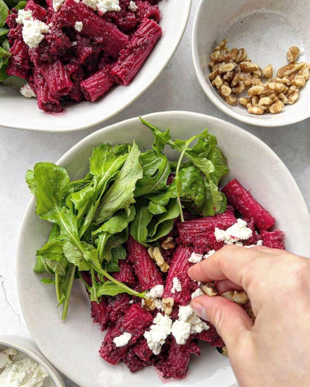 A bowl of beetroot goat cheese pasta being topped with a sprinkle of walnuts.