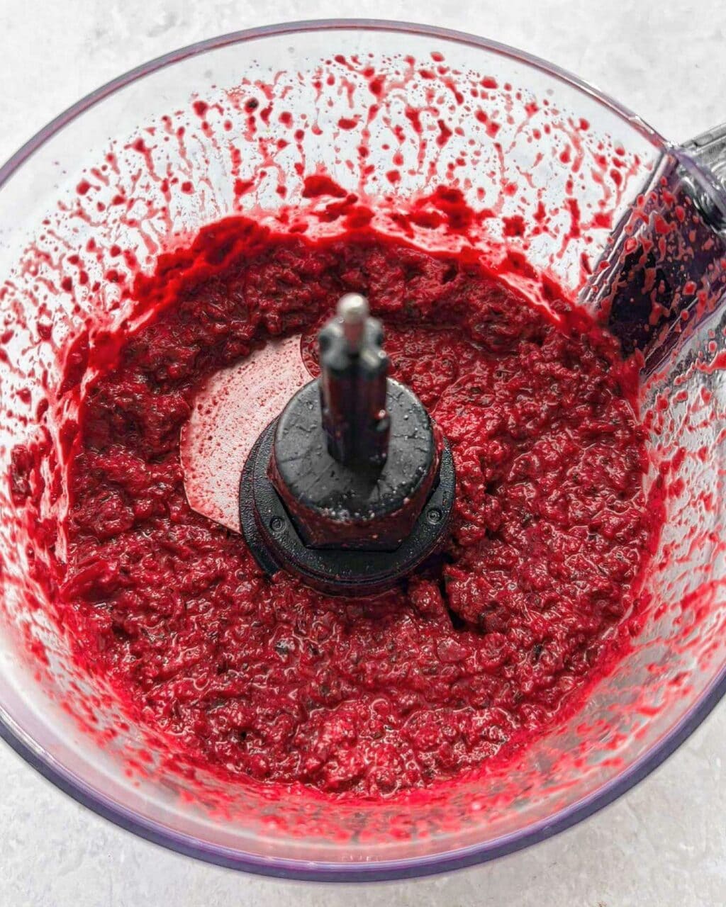 A food processor with a sauce made with the beetroot, goat cheese, lemon, salt and pepper, and garlic.