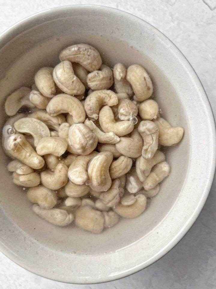 Cashew nuts being soaked in a bowl of hot water.