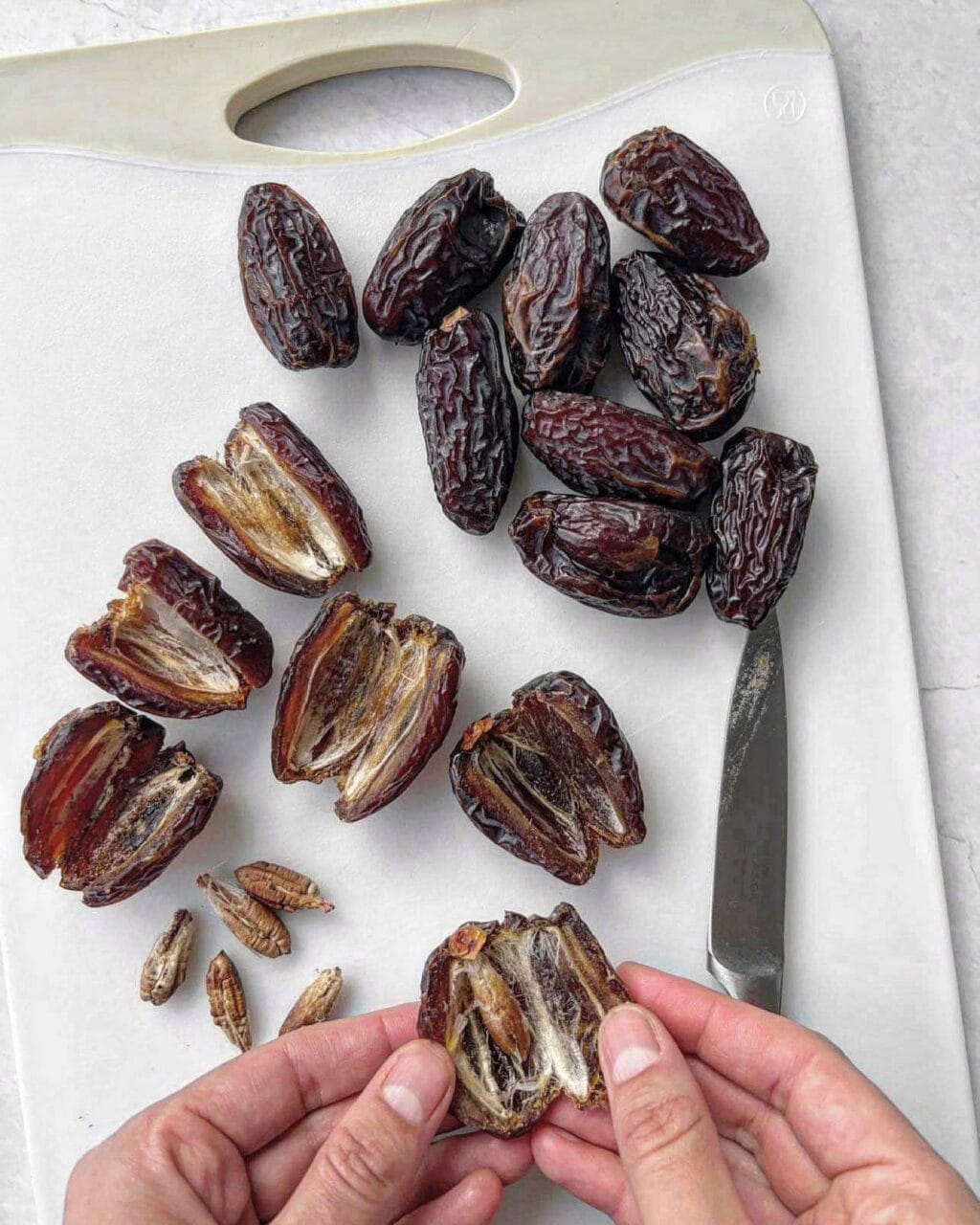 Medjool dates on a chopping board. Some are whole and some are sliced open with the pit removed.