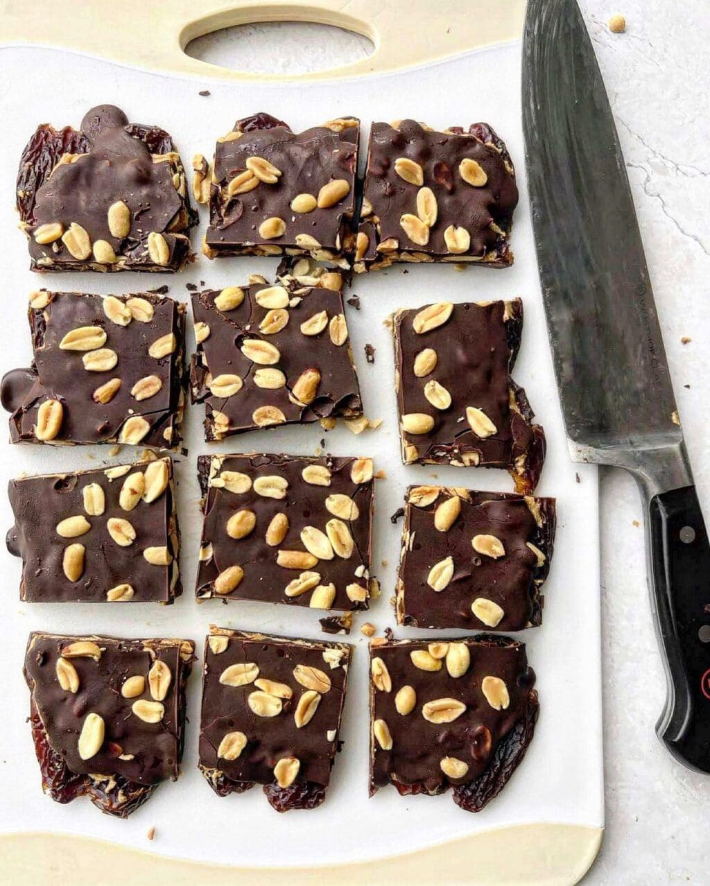 Twelve squares of chocolate date bark on a chopping board with a chef knife.
