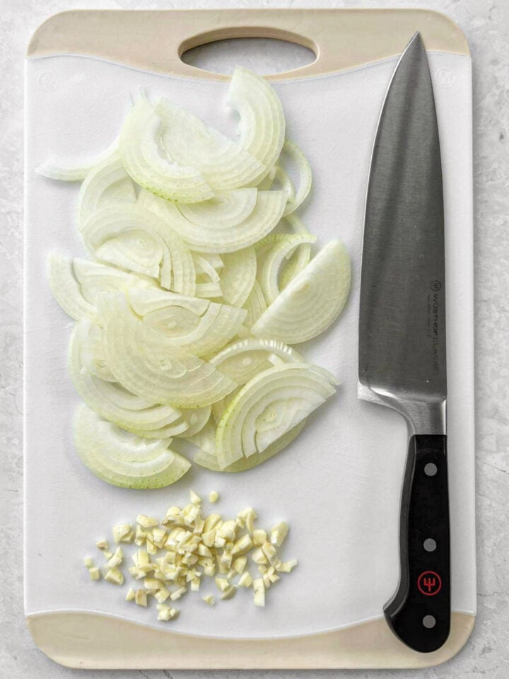 Sliced onions and chopped garlic on a chopping board.