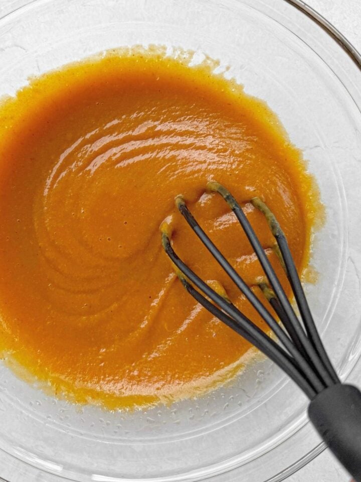 Whisk together the wet ingredients to making pumpkin pecan muffins, including pumpkin puree, maple syrup, olive oil, egg and vanilla.
