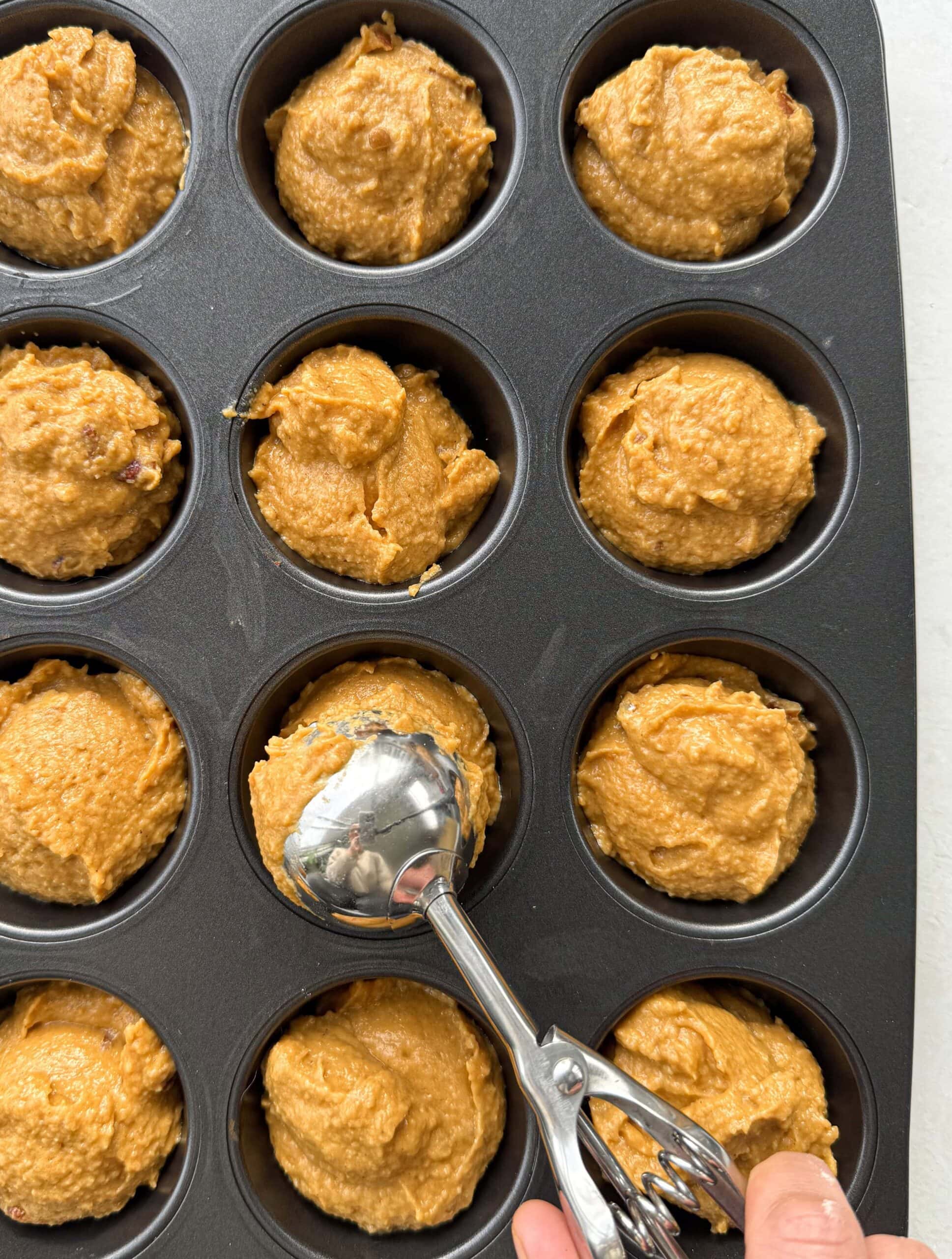 Scooping the batter into a 12-hole muffin tray using an ice cream scoop.